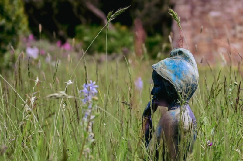 A metal statue of a small child in amongst grasses and flowers